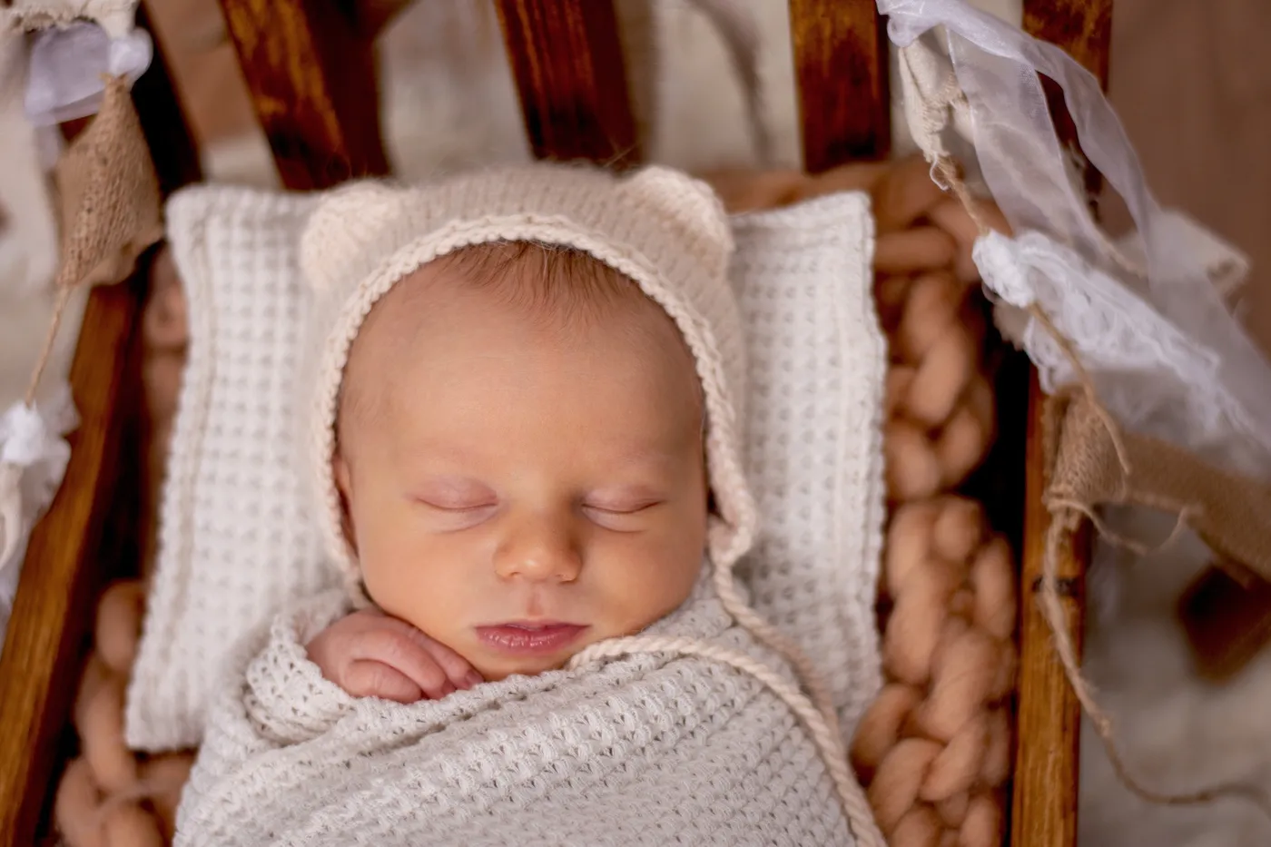 Schlafendes Baby mit heller Strickmütze in einer hölzernen Wiege