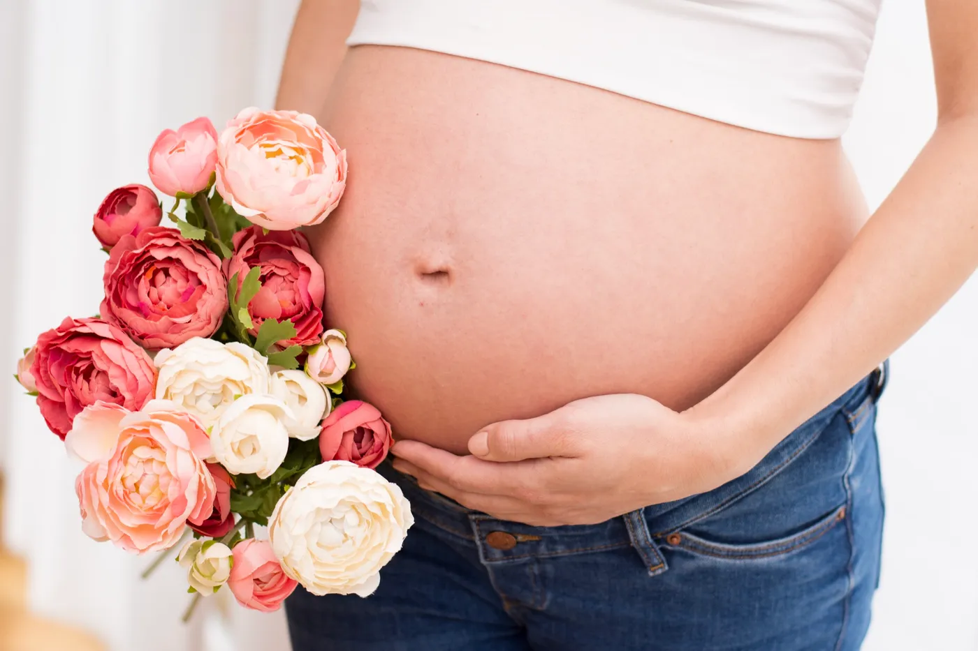 Babybauch in Nahaufnahme, daneben ein Strauß Pfingstrosen