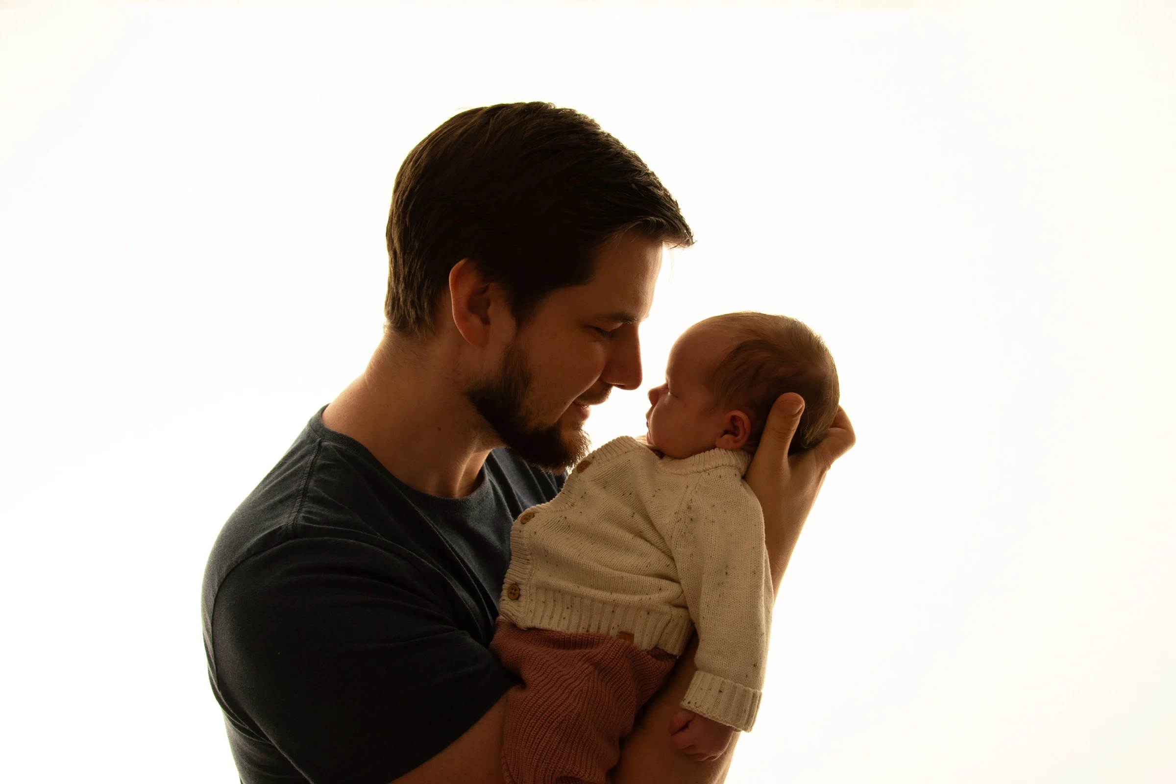 Ein Vater hält sein Neugeborenes im warmen Gegenlicht, Nase an Nase